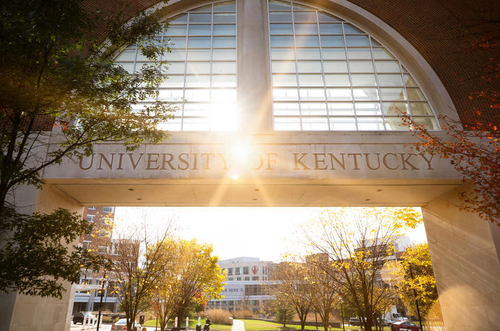 Picture of the sun shining through a glass structure with the words "University of Kentucky" carved into stone."
