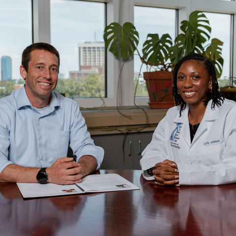 Two people sitting at a desk, posing for a photo. 