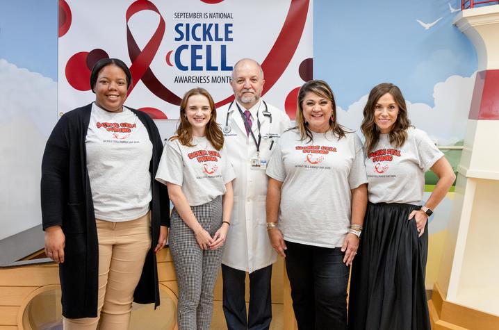 Four women and one man posing for a picture wearing matching shirts that say "sickle cell strong."" 