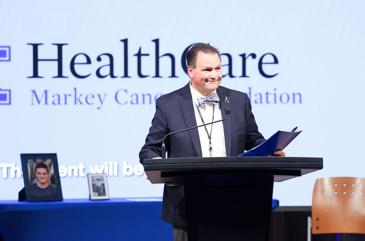 Man standing behind a podium holding a folder. 