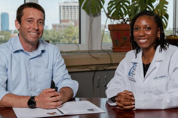 Two people sitting at a desk, posing for a photo. 