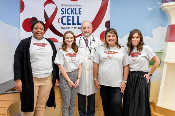 Four women and one man posing for a picture wearing matching shirts that say "sickle cell strong."" 