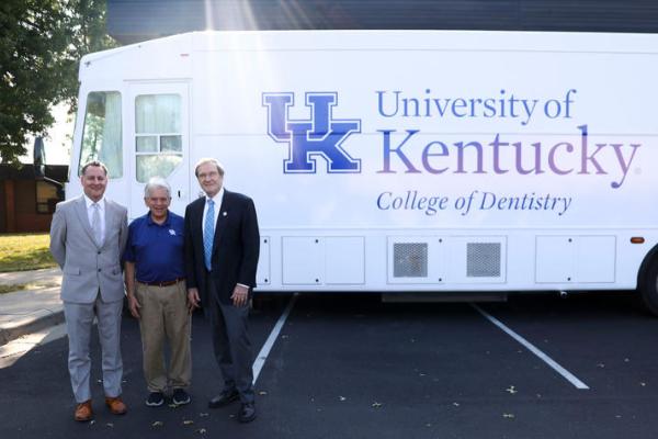 Three men standing in front of a white dentistry van.  