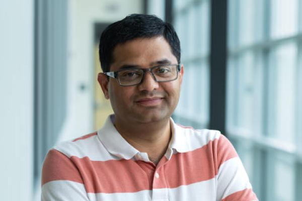 Man in a orange and white striped shirt with his arms crossed, smiling at the camera.