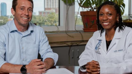 Two people sitting at a desk, posing for a photo. 