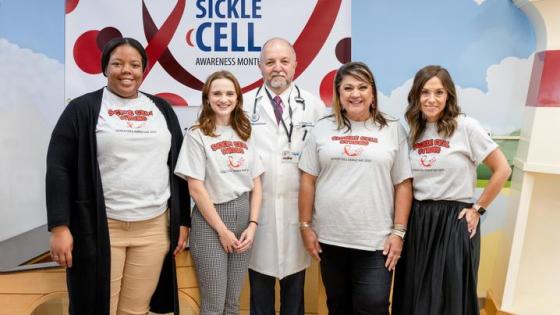 Four women and one man posing for a picture wearing matching shirts that say "sickle cell strong."" 