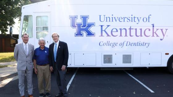 Three men standing in front of a white dentistry van.  