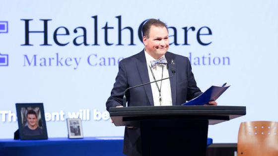 Man standing behind a podium holding a folder. 