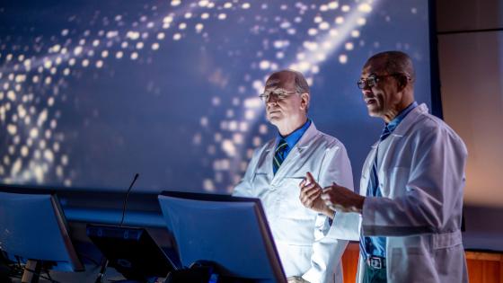 Two men in white lab coats looking at a computer.