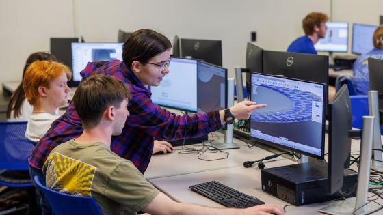 Three students looking and pointing at a computer screen.